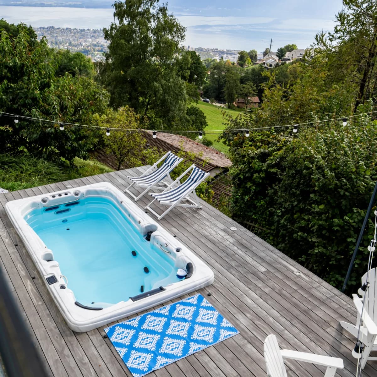 Spa de nage sur une grande terrasse en bois, transats et guirlande lumineuse