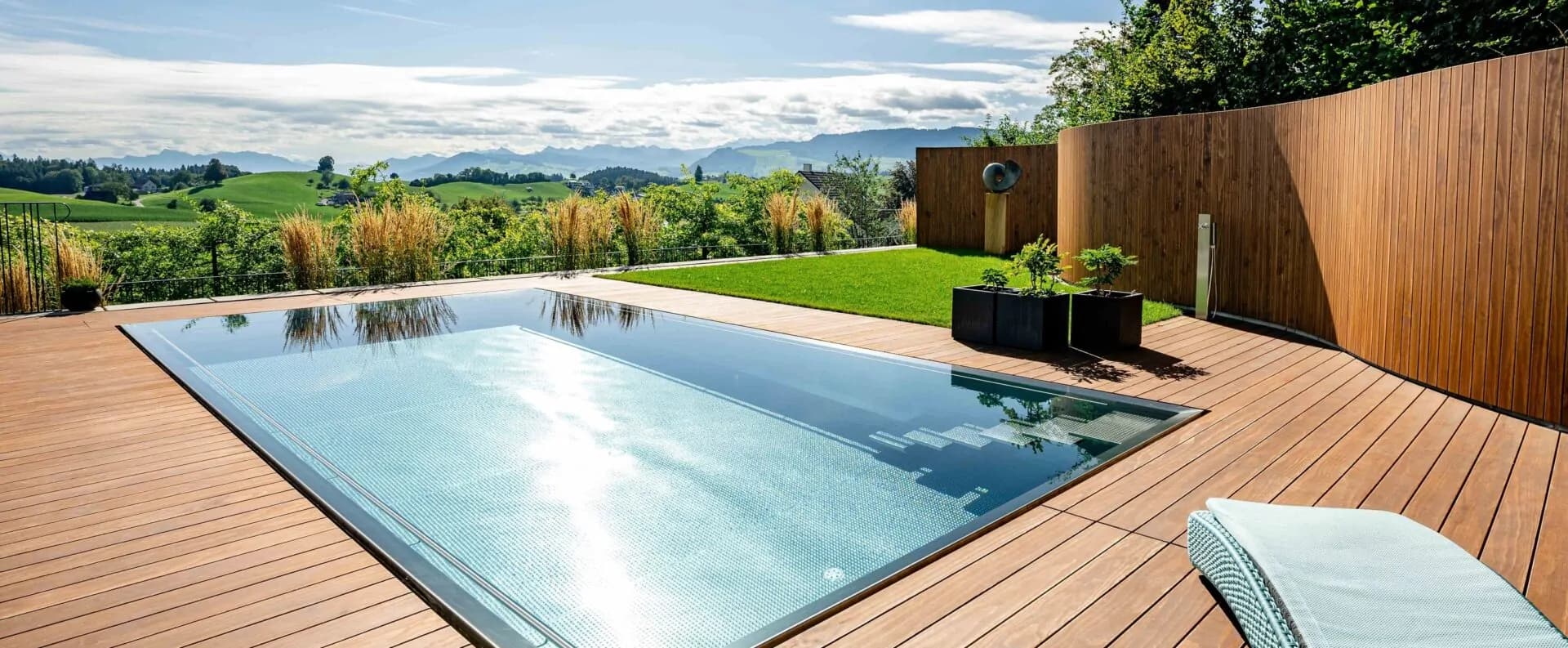 Grande terrasse en bois Accoya avec bassin miroir face aux collines, en plein soleil