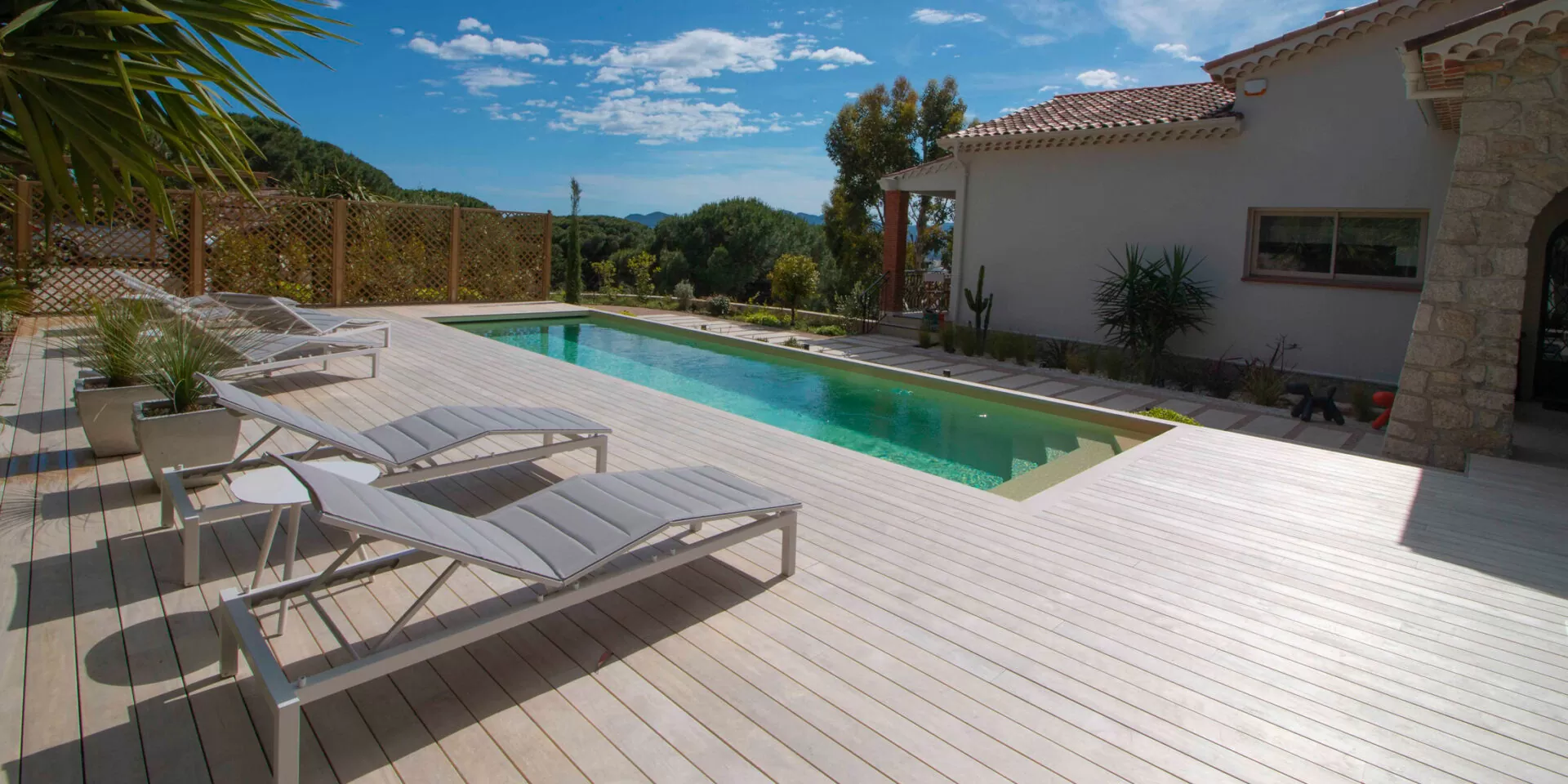 Terrasse en bois Accoya naturel autour d’une piscine de villa, transats au soleil
